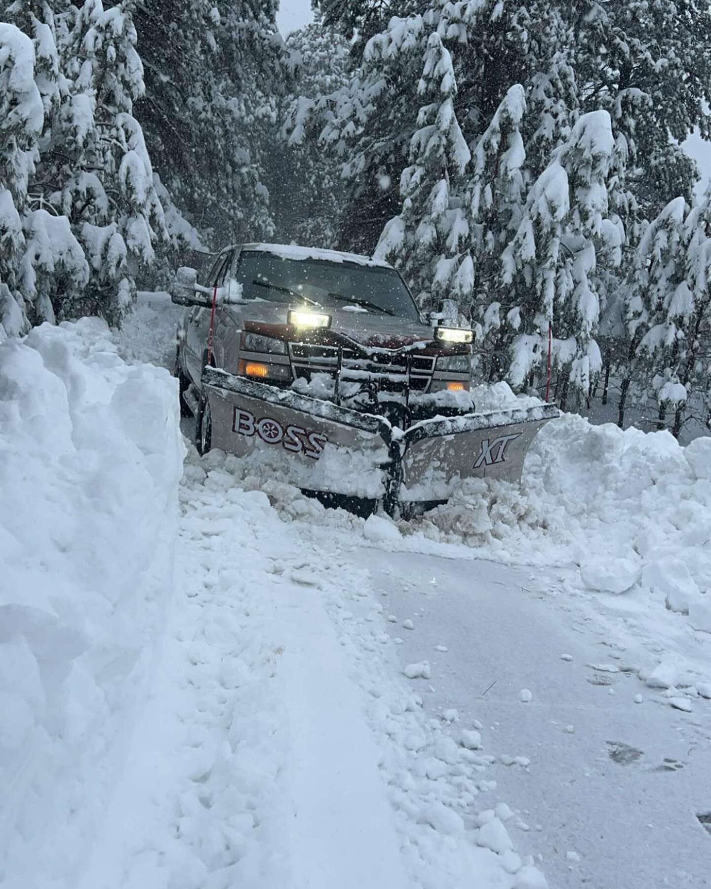 A snow plow is driving down a snow covered road.