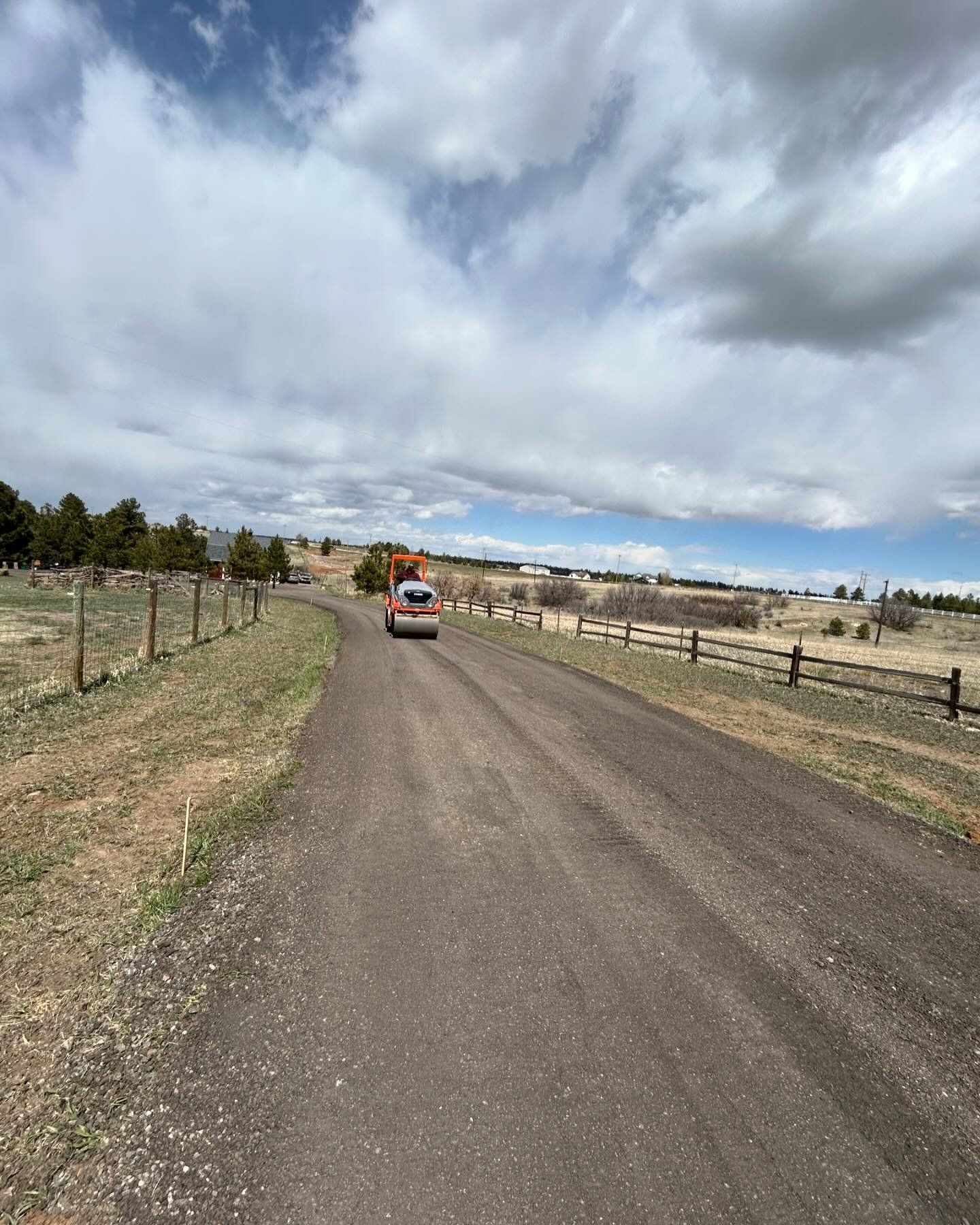 A car is driving down a dirt road next to a fence.