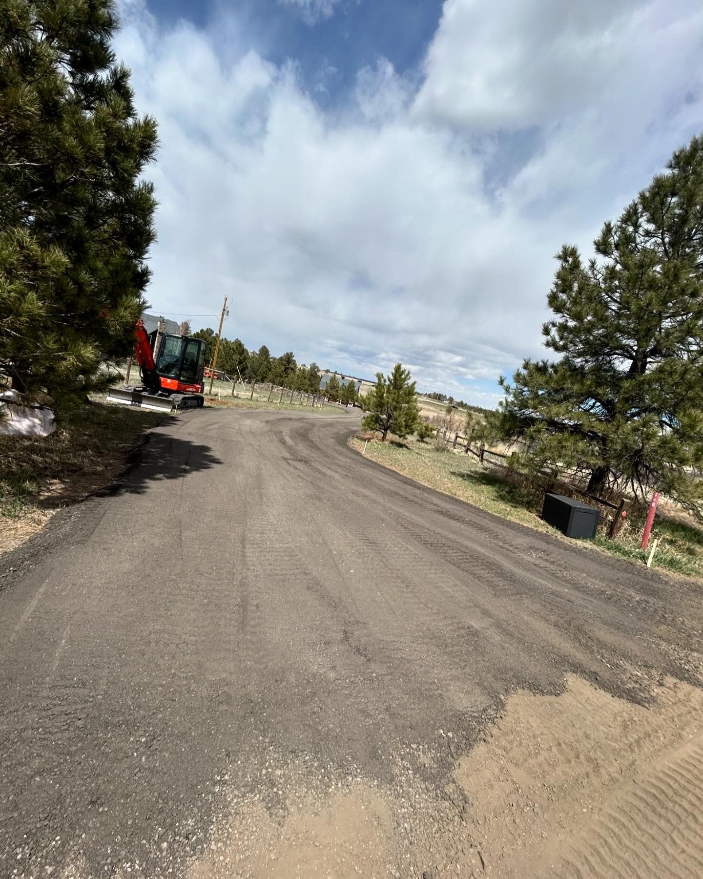 A tractor is driving down a dirt road next to trees.