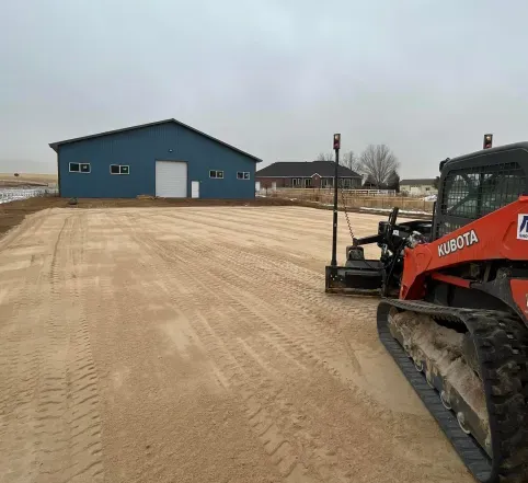 A red and black bulldozer is sitting in the dirt in front of a blue building.