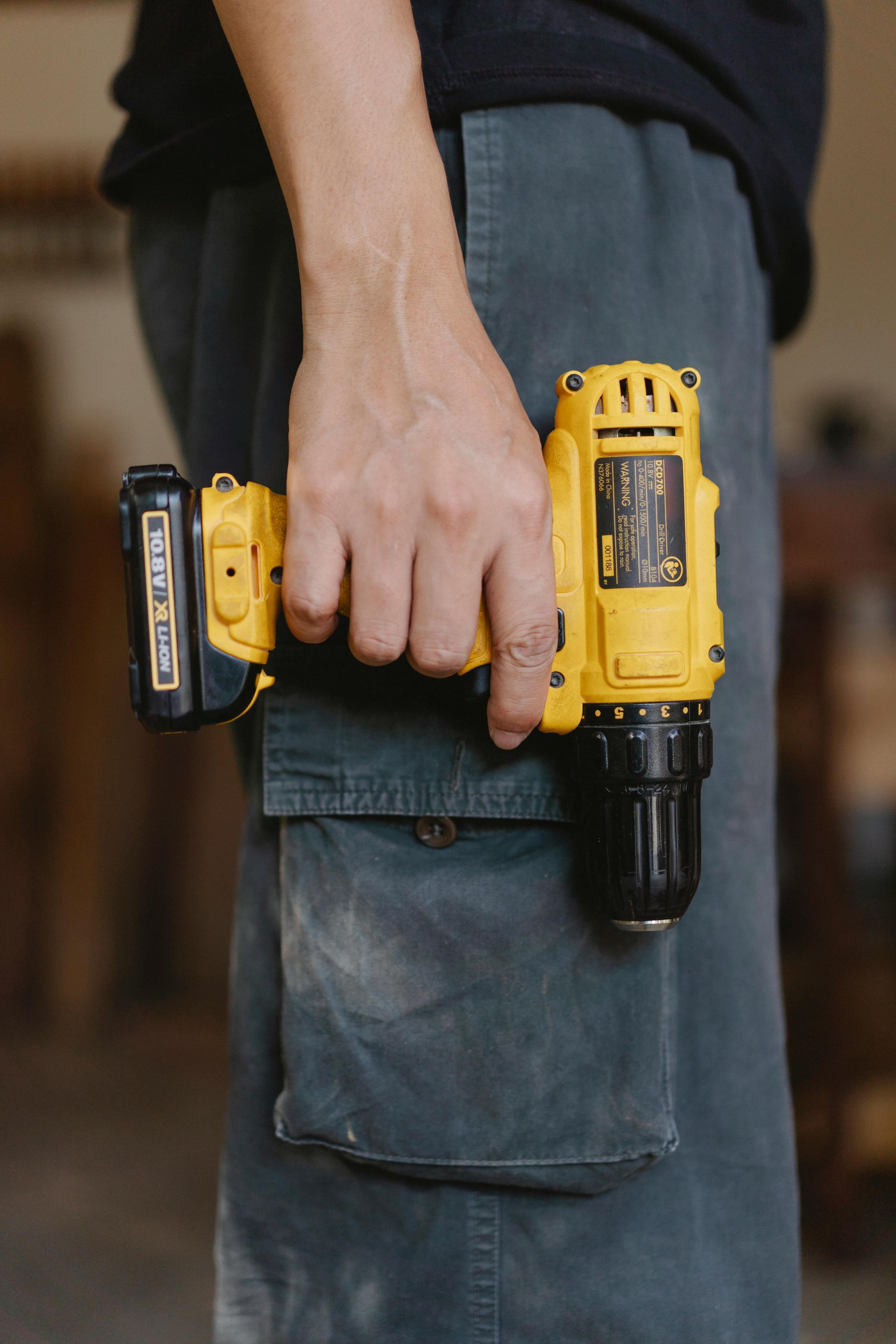 Person holding a yellow and black cordless drill against gray work pants.