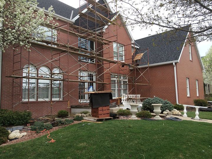 A large brick house with scaffolding around it is being painted.
