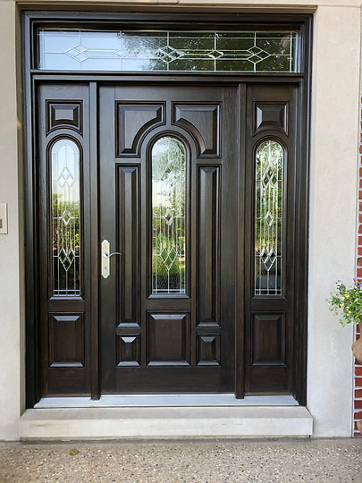 A large wooden door with stained glass windows is on a brick wall.