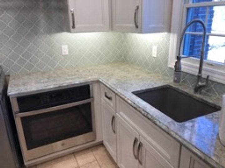 A kitchen with white cabinets , a stainless steel oven , a sink , and a window.