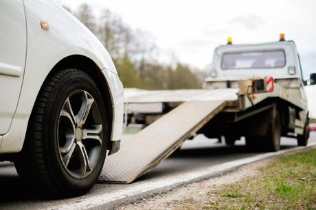 Grey Suv loaded up on flat bed tow truck being driven on the road