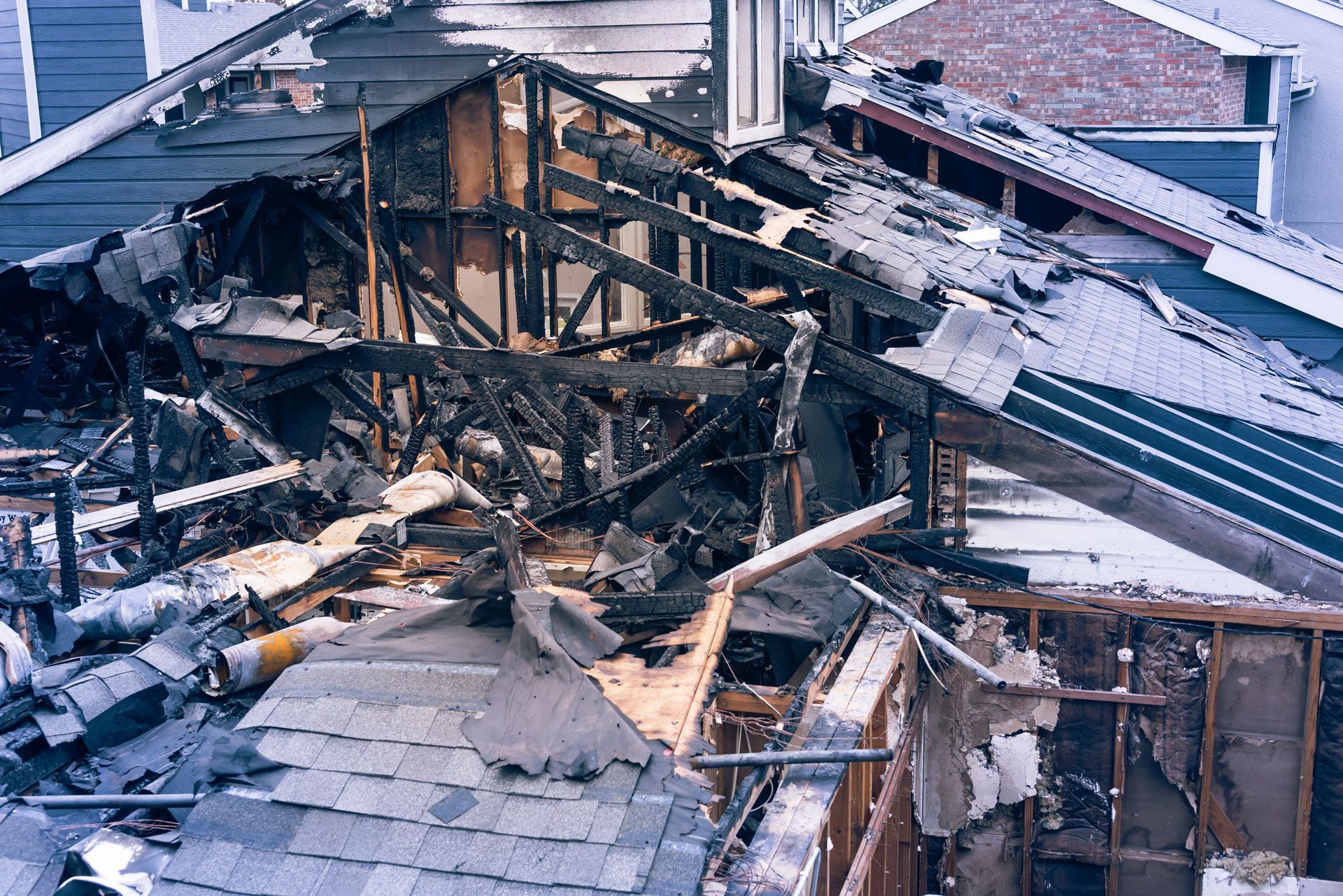 Charred remains of a house roof after a fire, showing exposed beams and debris.