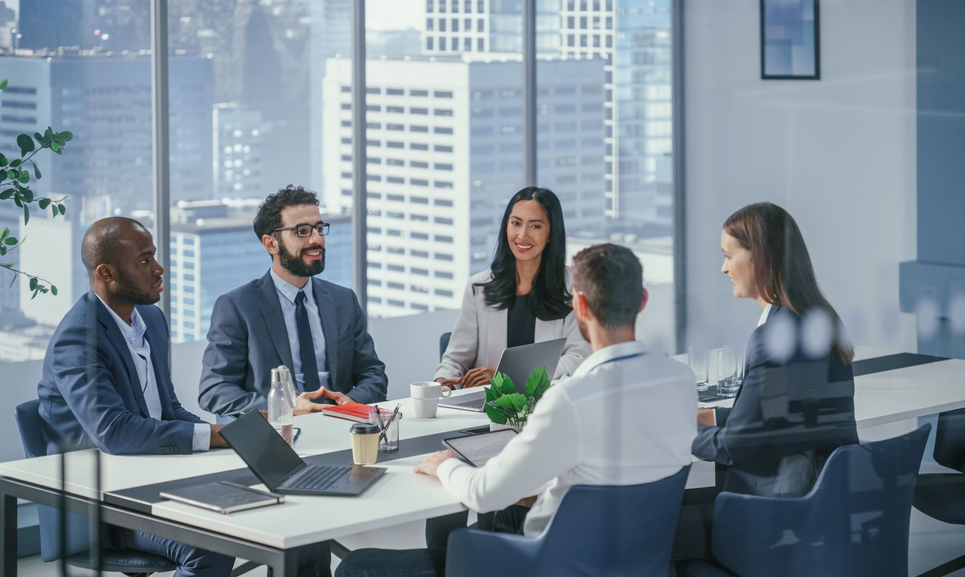 Business colleagues at a conference table with city backdrop, discussing strategy.
