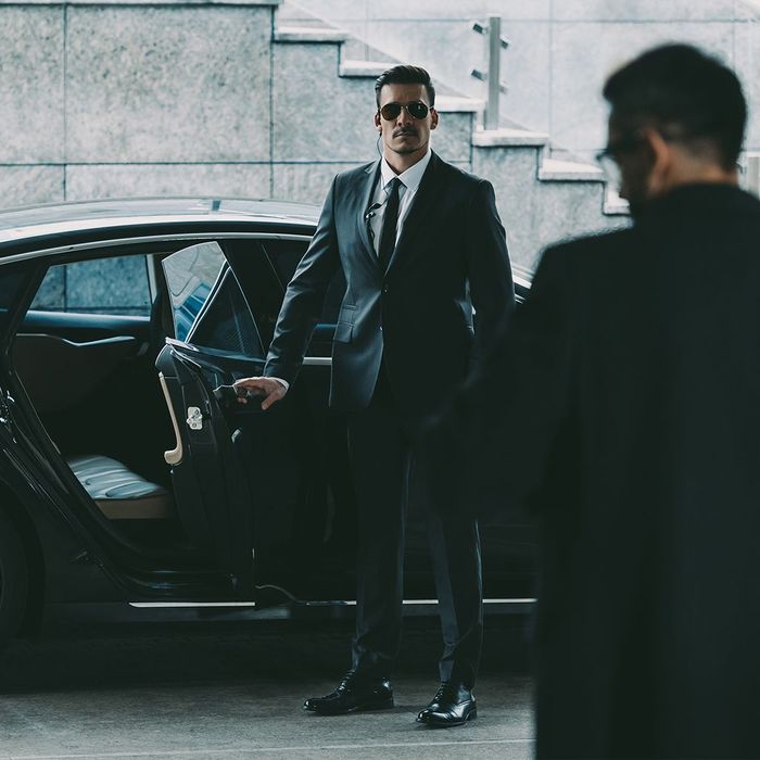 A man in a suit and tie is standing next to a car.