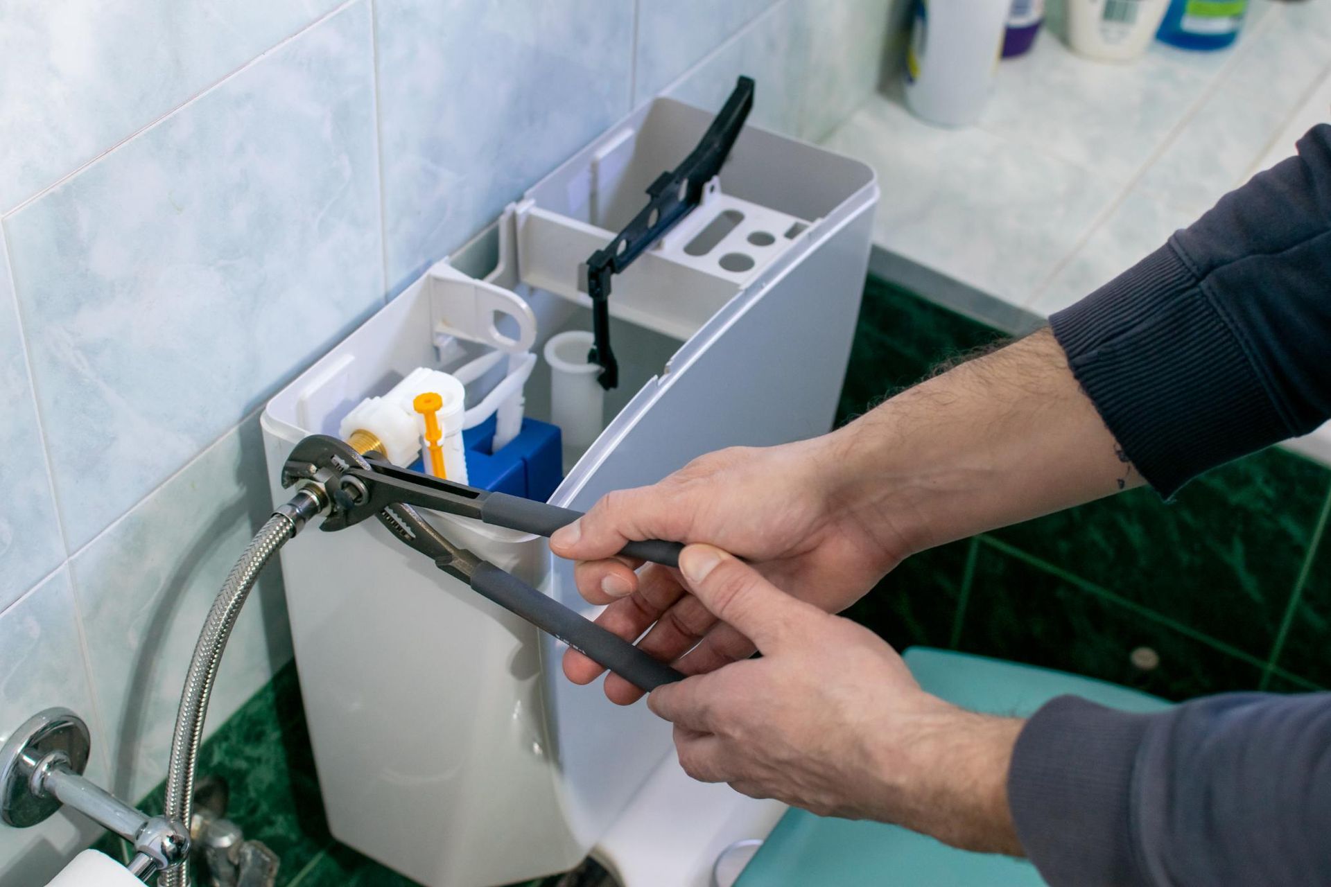 Person using pliers to work on the internal components of a toilet tank.