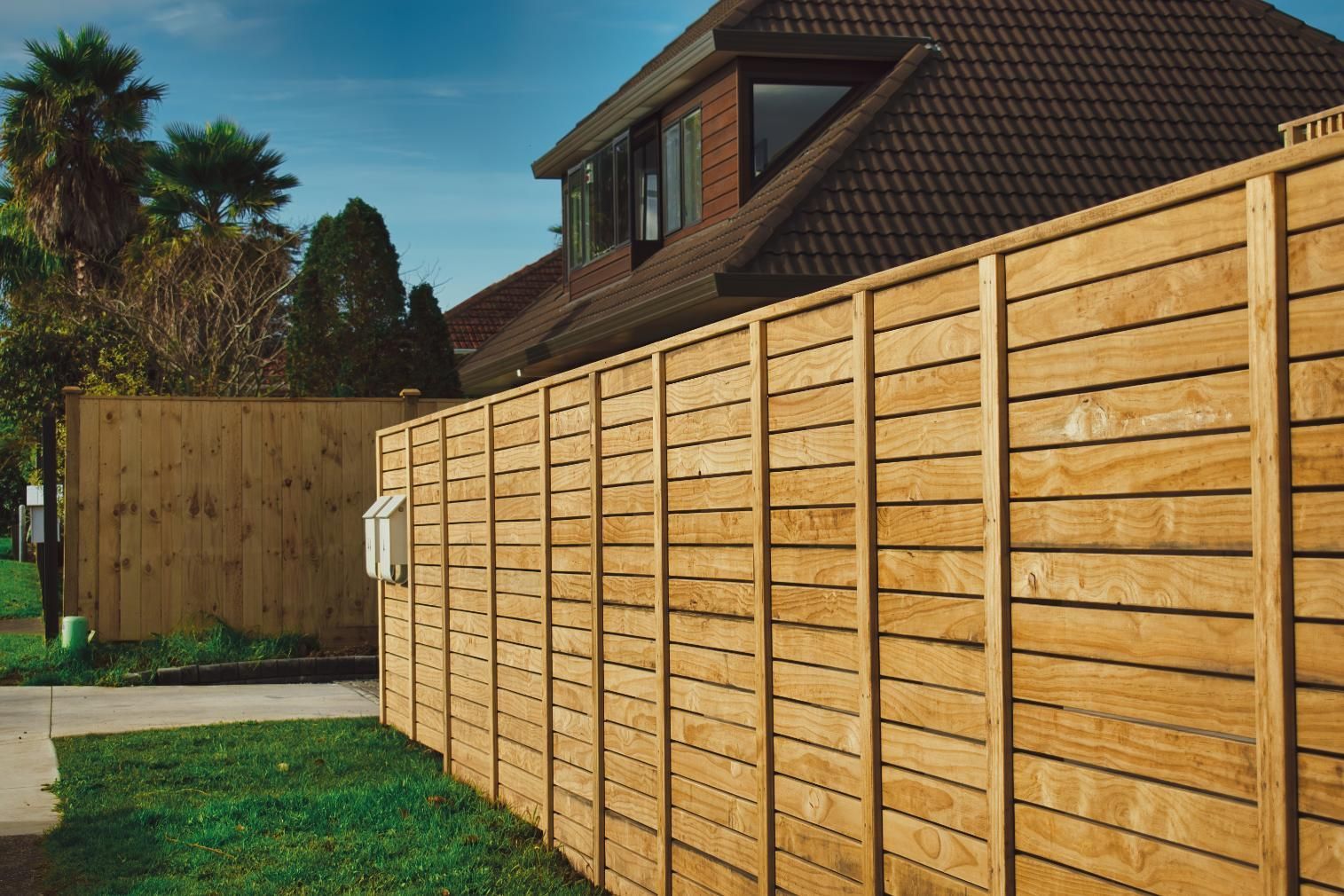 Wooden fence surrounding a house with a brown roof and a small green lawn.