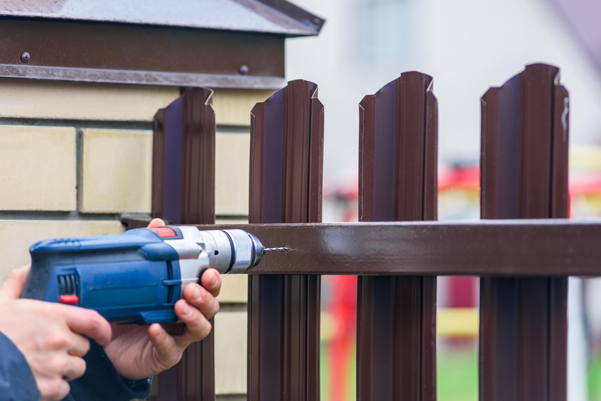 Person using a drill to install a brown metal fence.