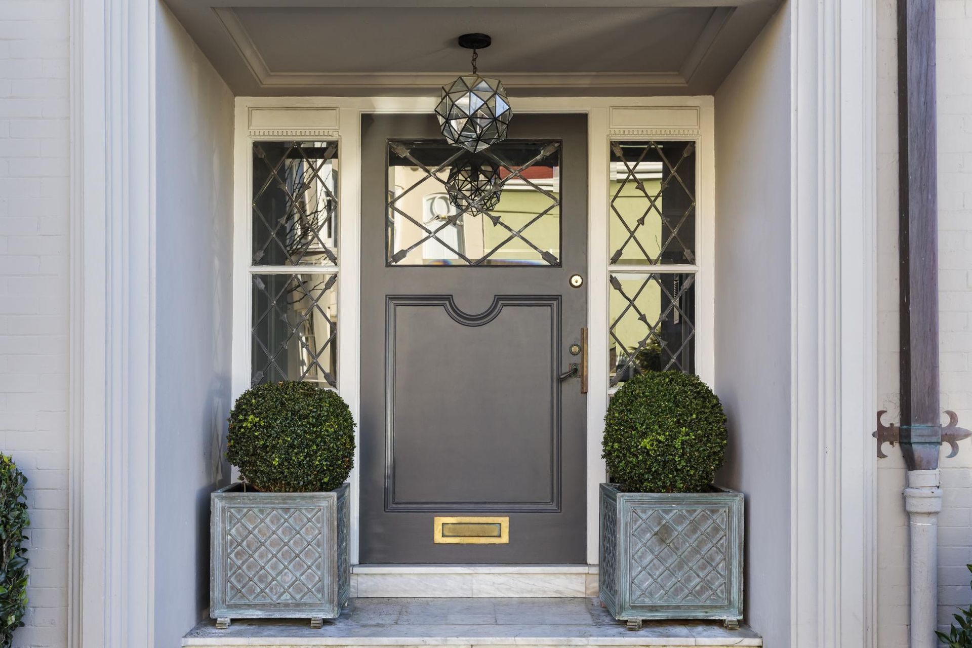 Gray front door with sidelights, decorative planters, and hanging light.