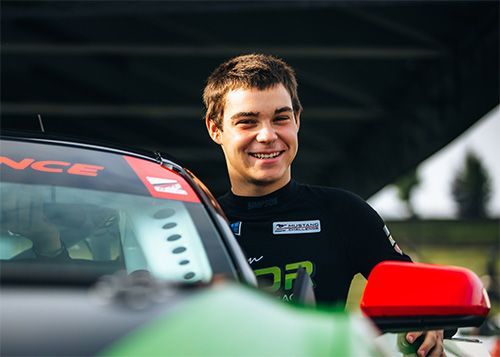 Max Opalski is standing next to a race car and smiling.