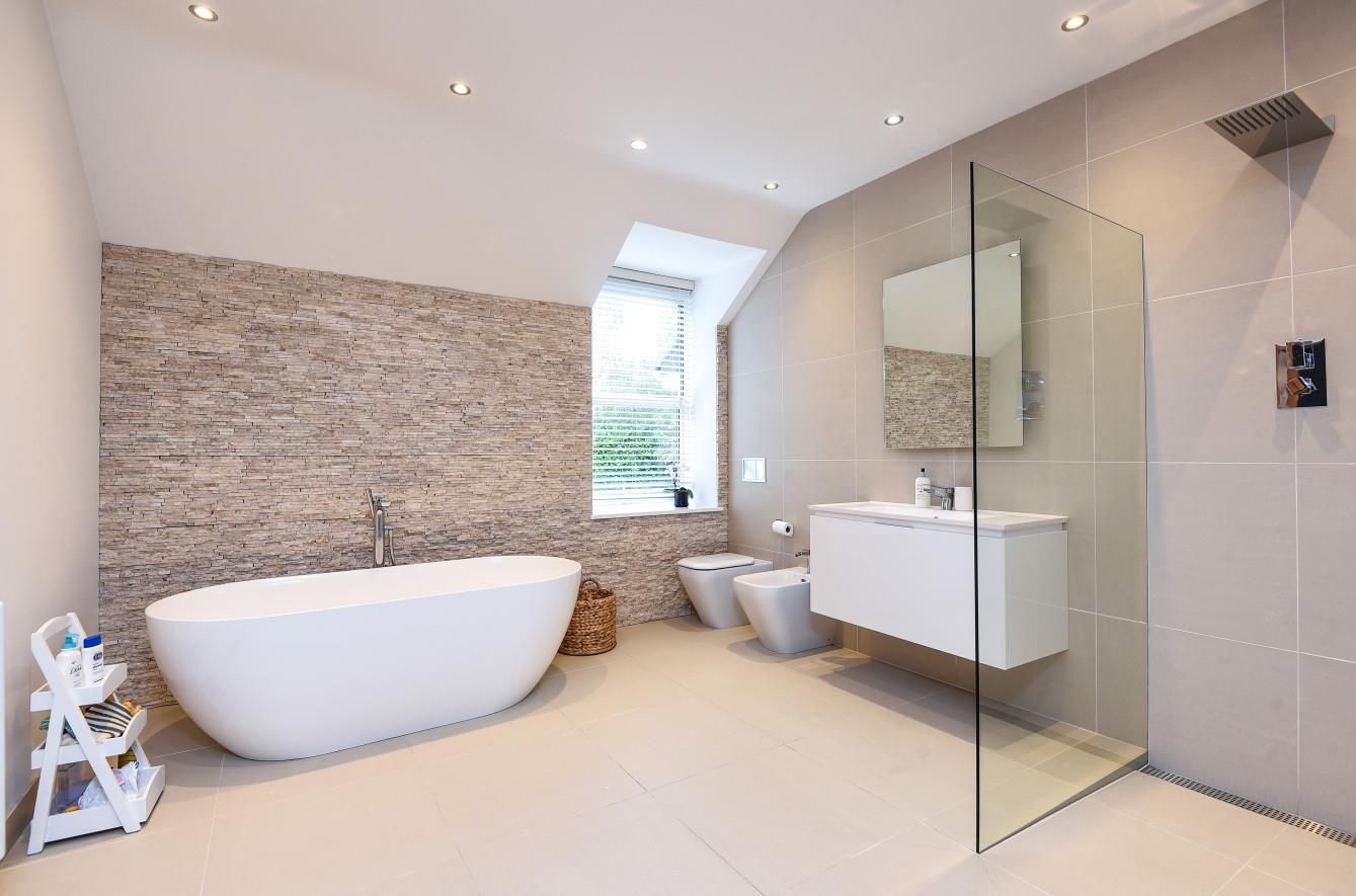 Modern bathroom with white tub, walk-in shower, floating vanity, stone accent wall, and beige tile.