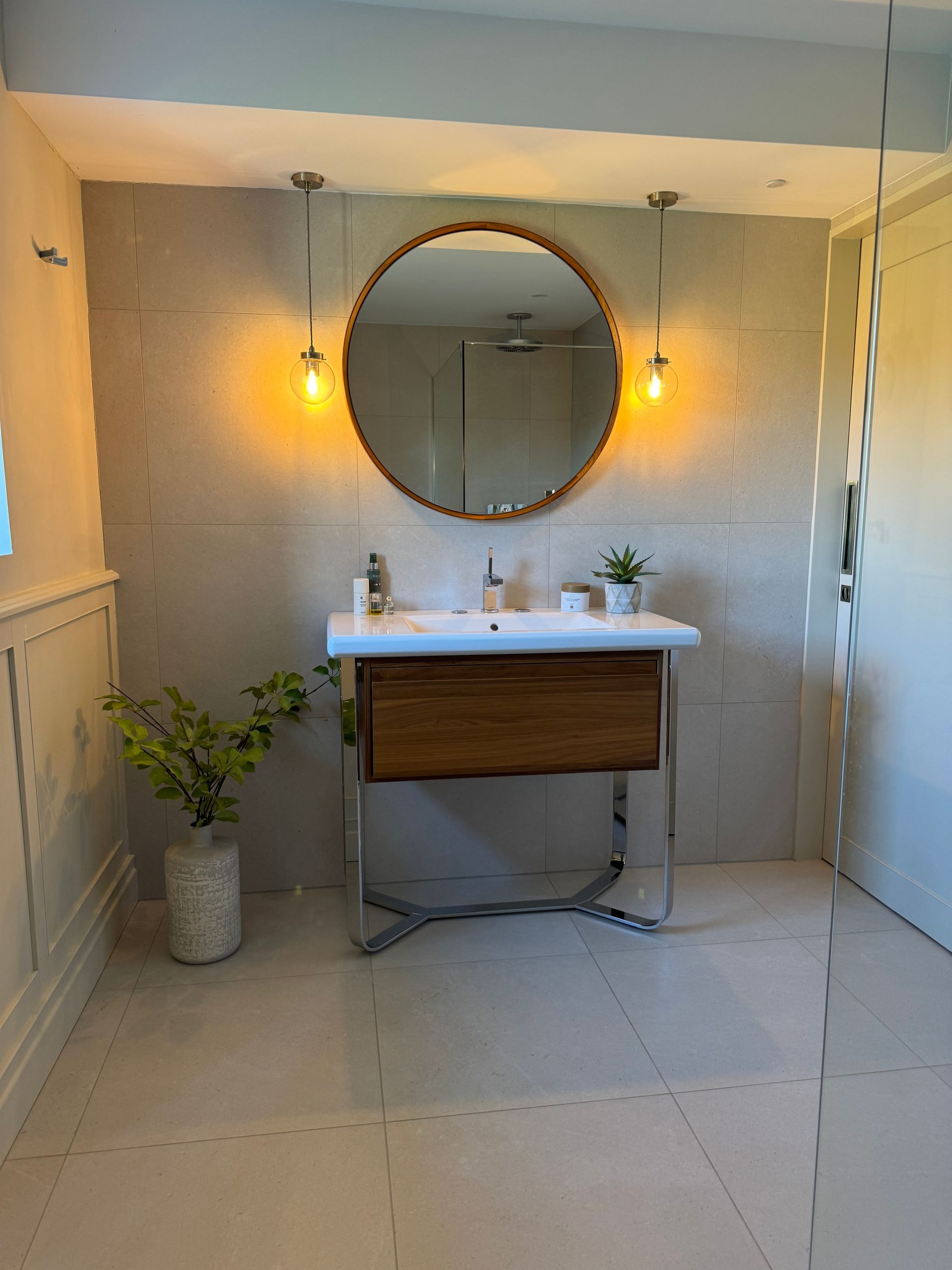 Bathroom with a round mirror, wooden vanity, and chrome legs.  Lights flank the mirror.