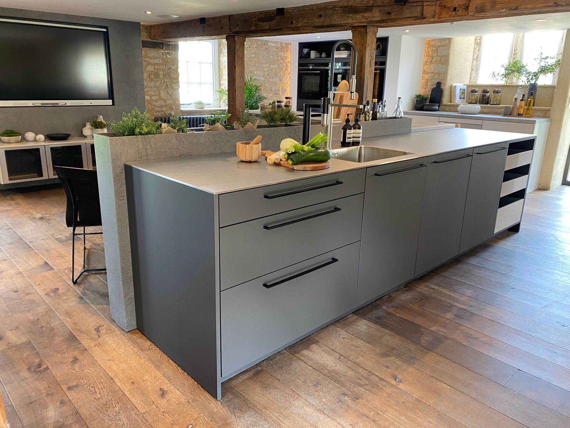 Modern gray kitchen island with sink and drawers; wooden floor, rustic beams.