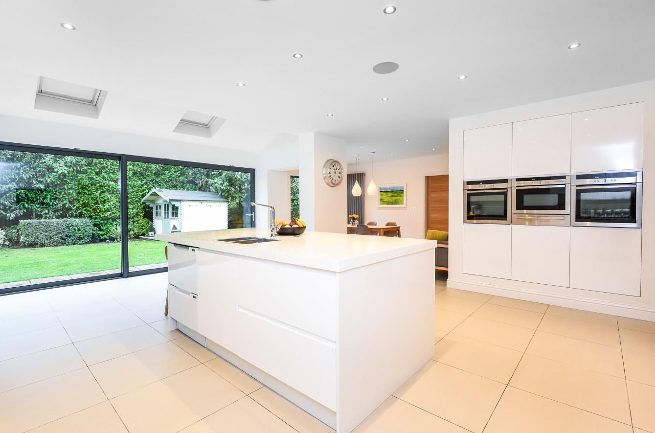 Modern, white kitchen with an island, stainless steel appliances, and a sliding glass door to a backyard.