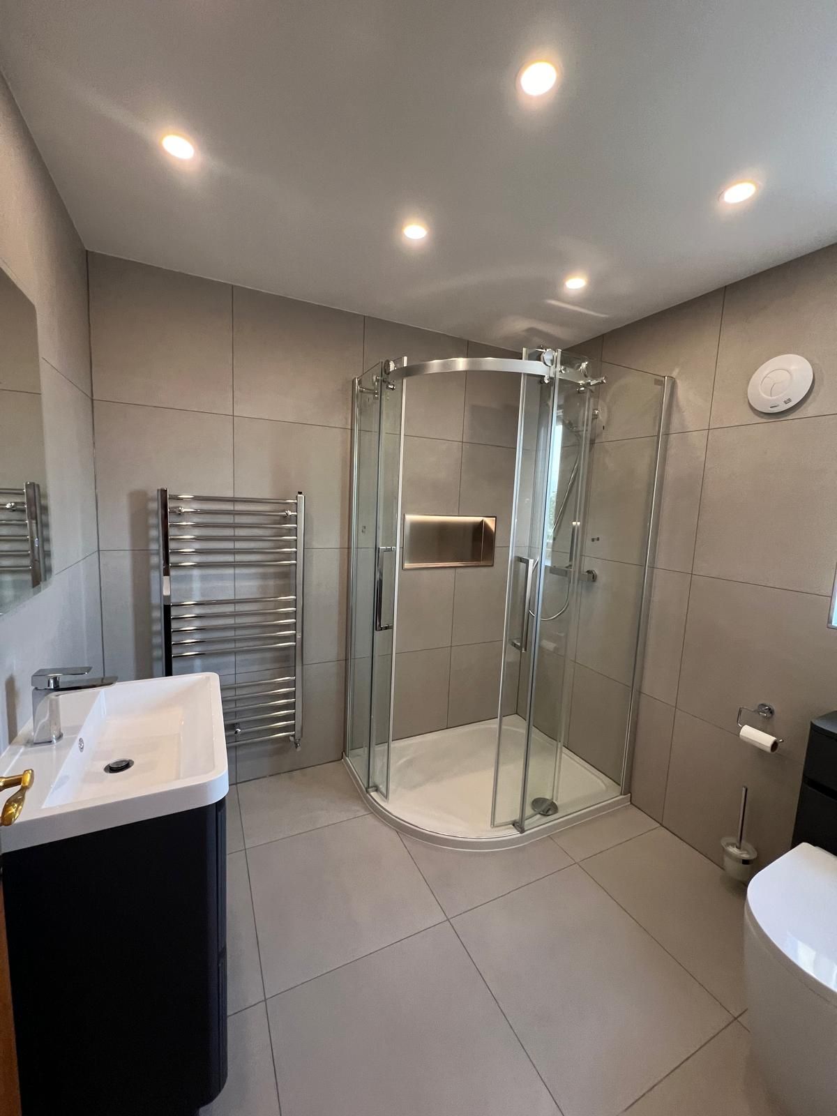 Modern bathroom with tiled walls, shower, vanity, heated towel rack, and toilet.