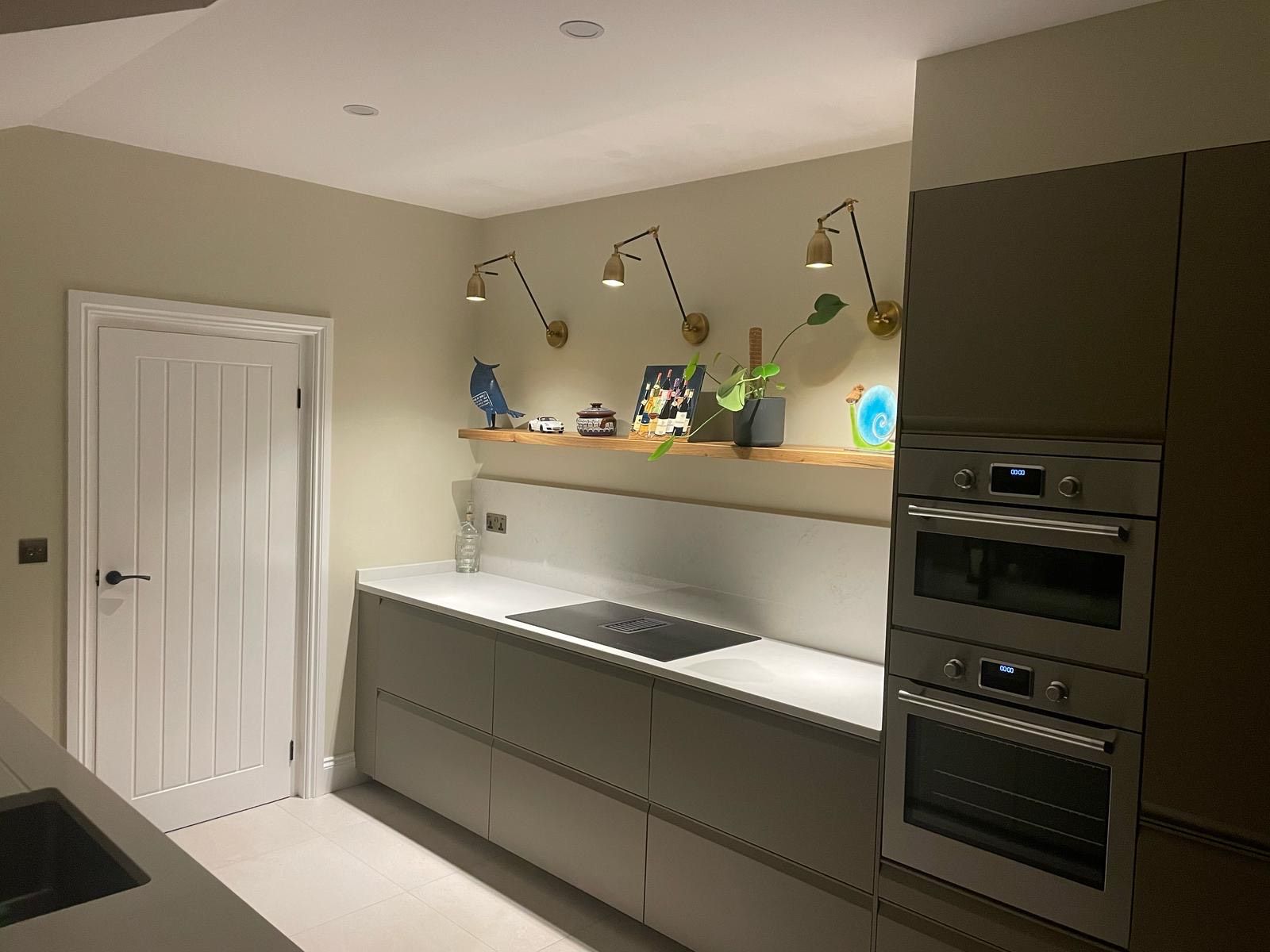 Kitchen with light gray cabinets, white countertop, open shelf with decor, and built-in ovens.