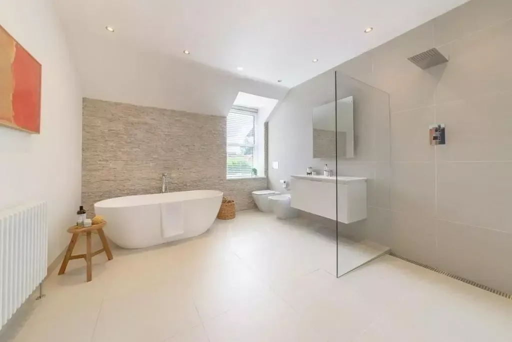 Modern bathroom with white tub, shower, and vanity. Neutral colors with textured wall and art.