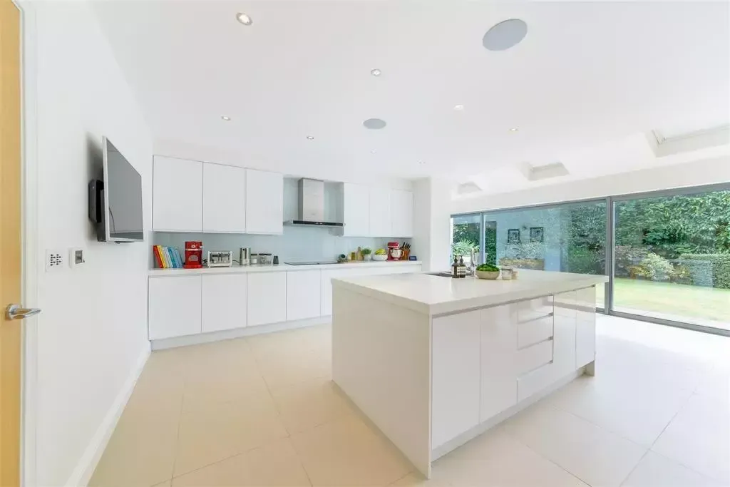 Bright white modern kitchen with an island, countertops, and large glass sliding doors overlooking a green yard.