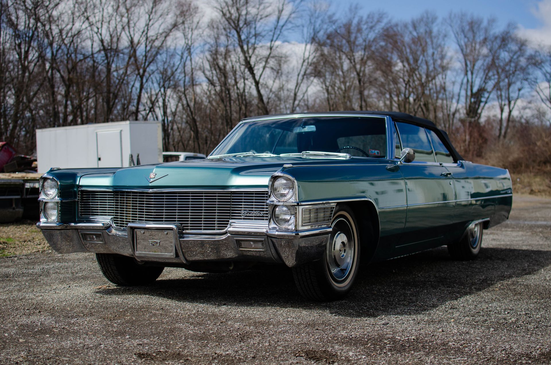 Teal 1966 Cadillac DeVille convertible parked on gravel.