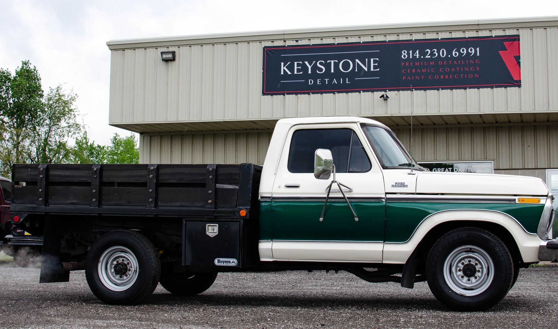 Vintage white and green flatbed truck parked in front of Keystone Detail business.