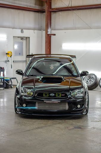 Black Subaru Impreza in a garage, showcasing modifications, with front view and focus on lights.