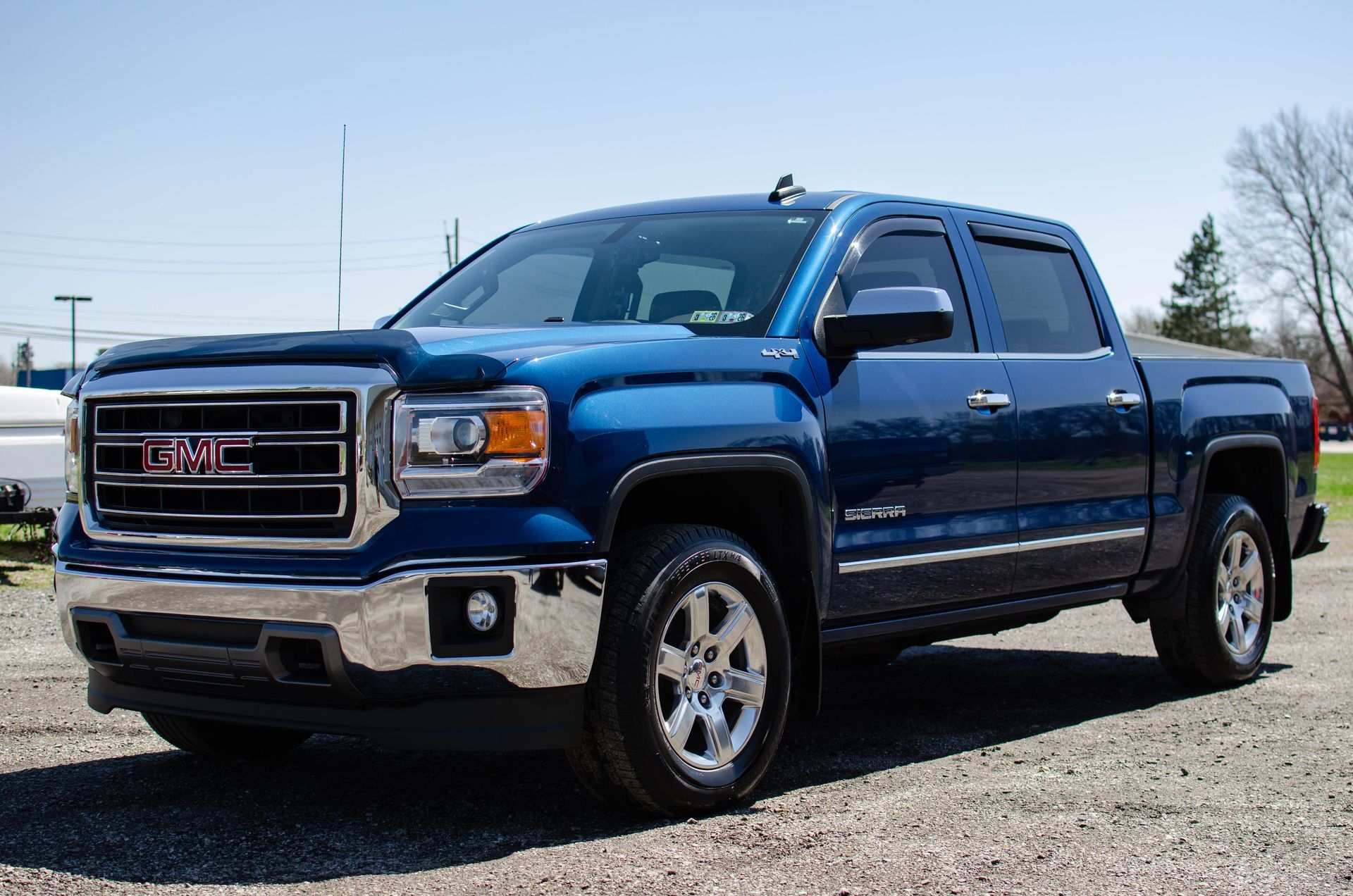 Blue GMC Sierra pickup truck parked on gravel. Sunny day.
