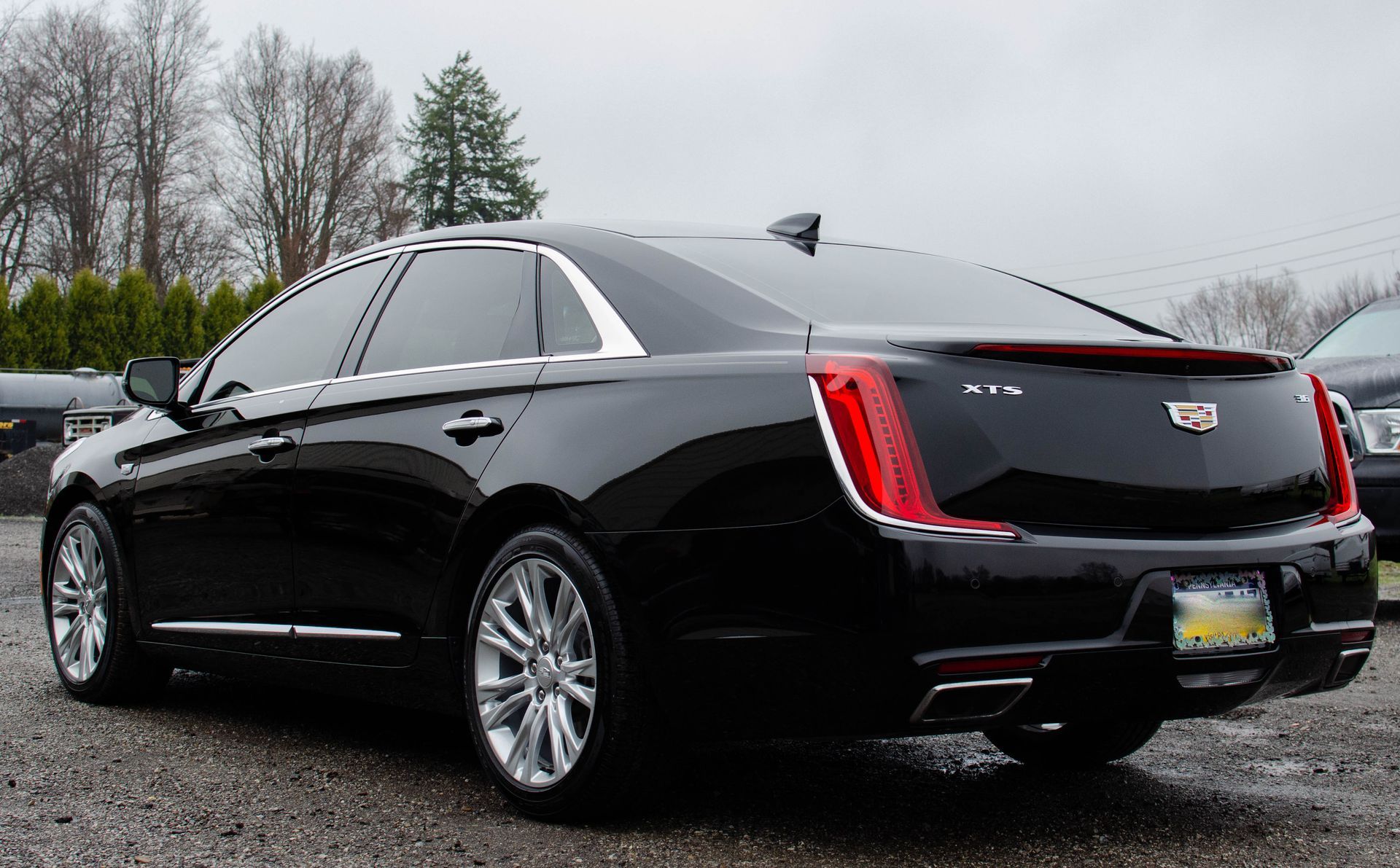Black Cadillac sedan parked on a wet, paved surface; cloudy sky.