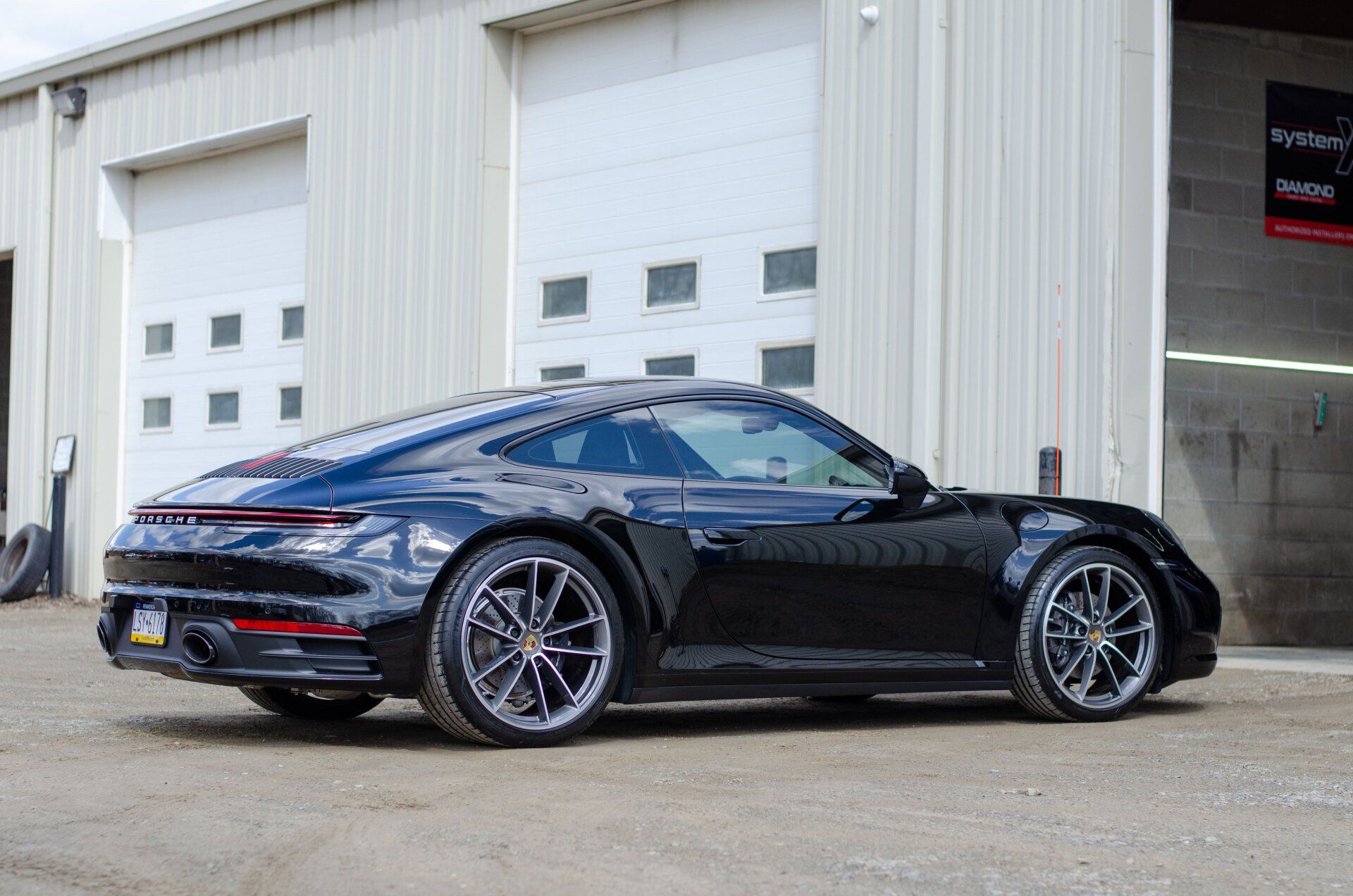 Black Porsche 911 parked in front of a white garage with two overhead doors.
