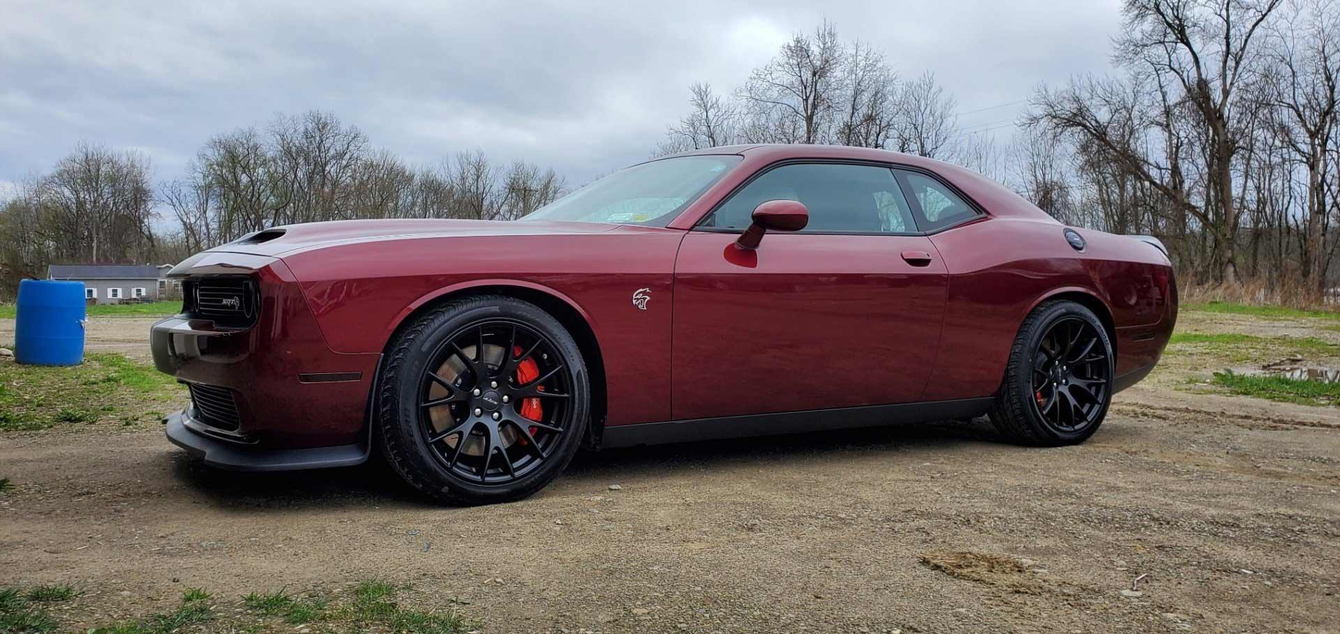 Maroon Dodge Challenger parked on a gravel road, with black rims and red brake calipers.