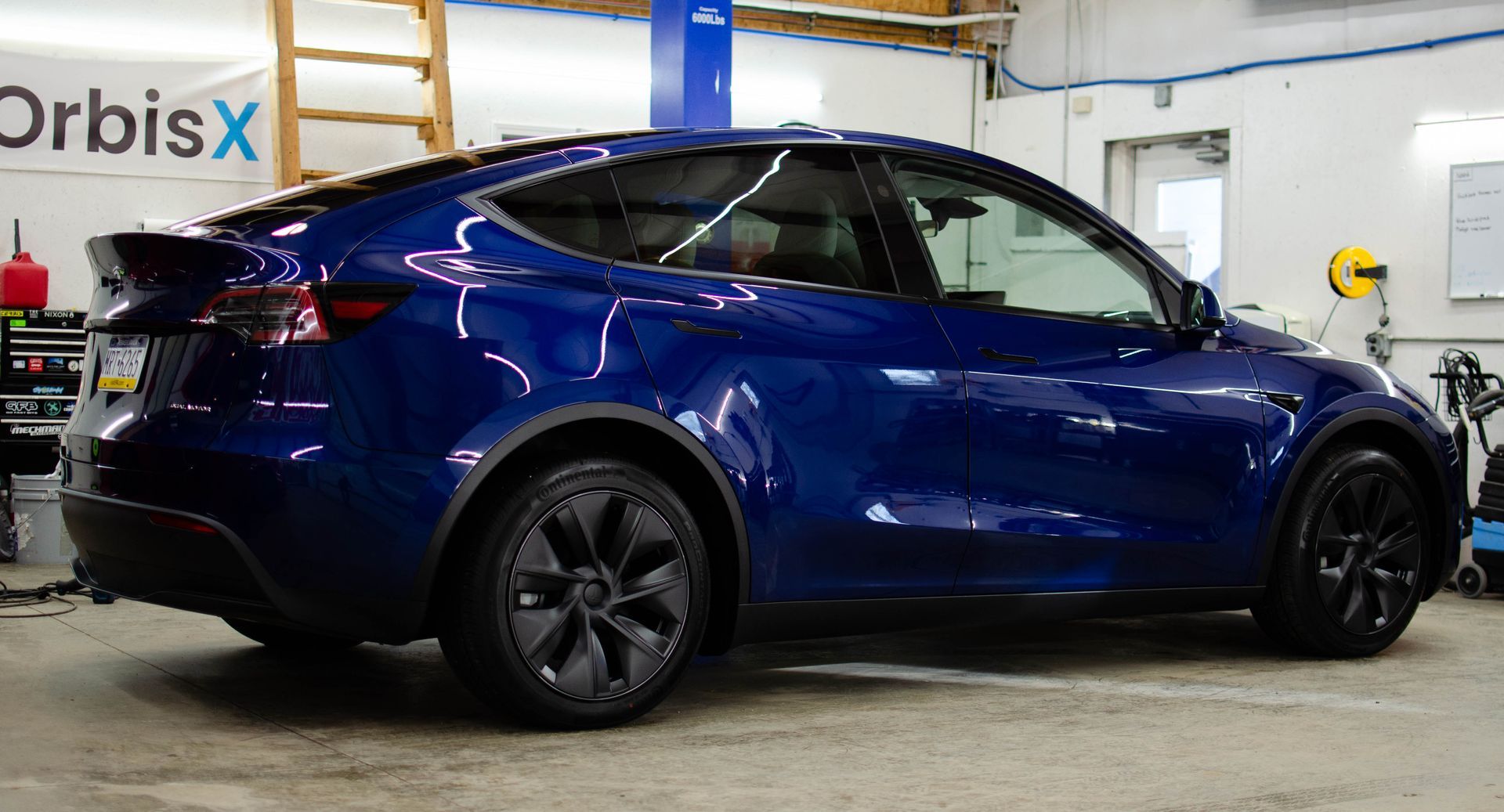 Blue Tesla Model Y with black wheels parked inside a garage.