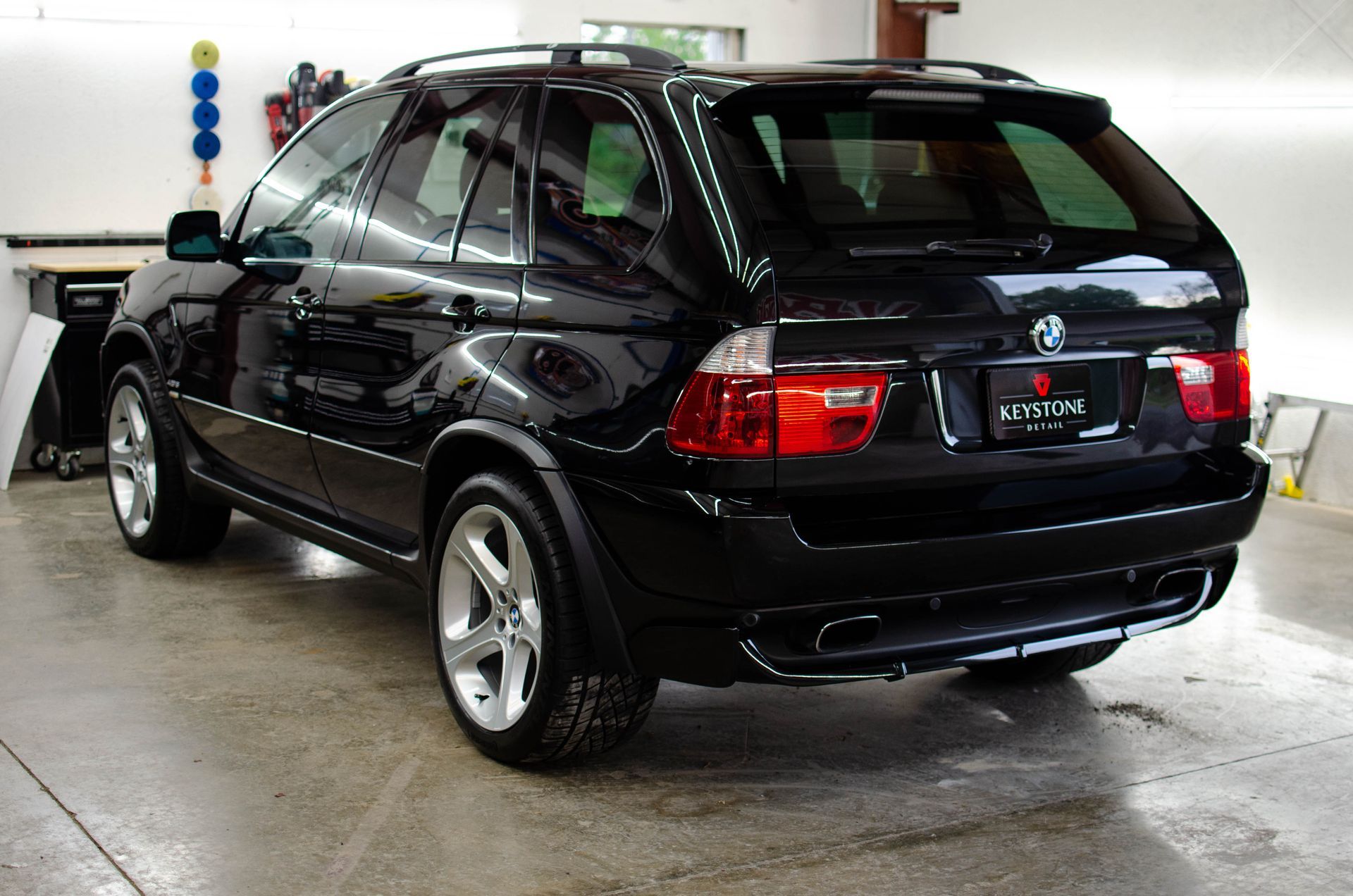 Black BMW X5 SUV parked in a garage, rear view. Silver wheels, tinted windows.