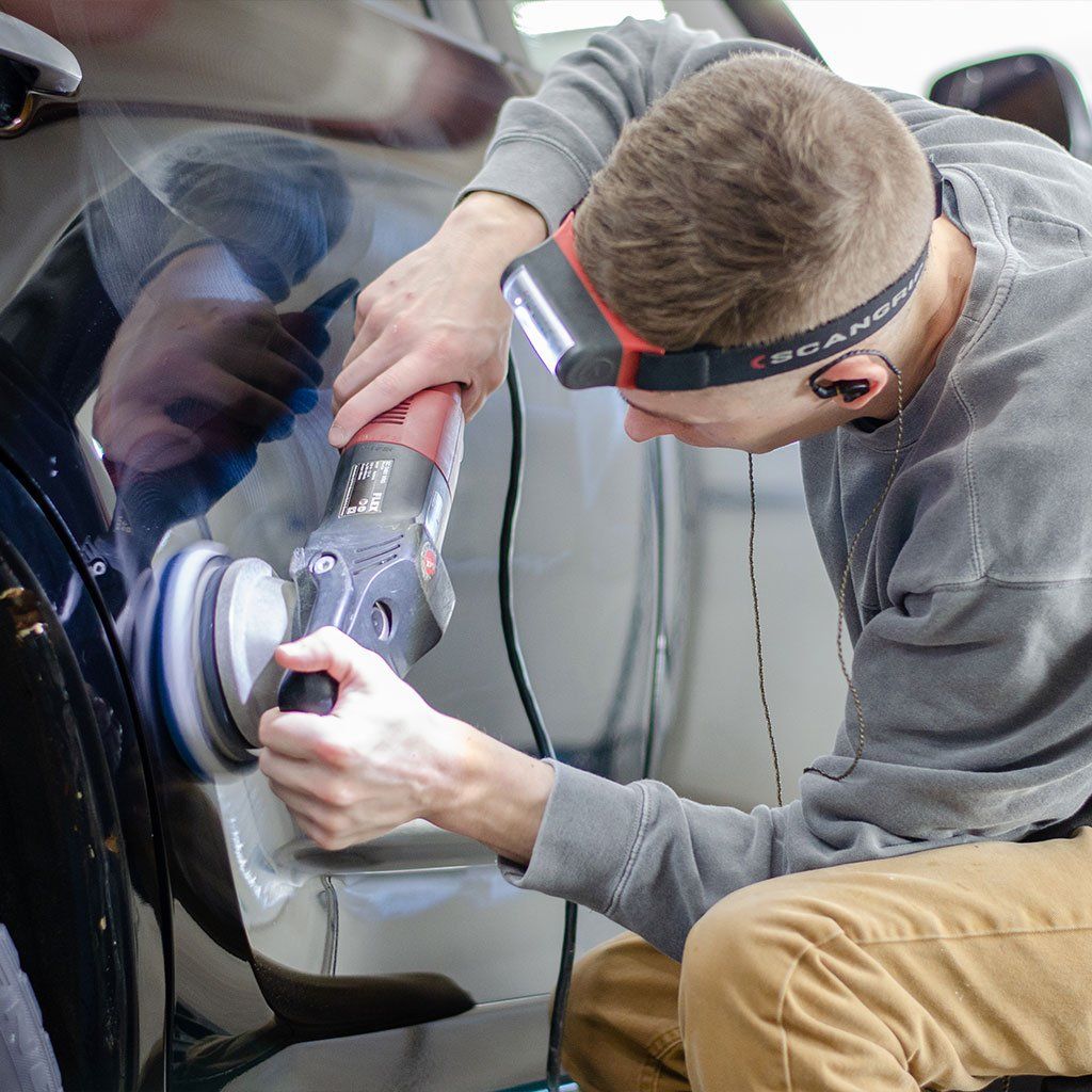 Man polishing a car, using an electric buffer, wearing a headlamp, indoors.