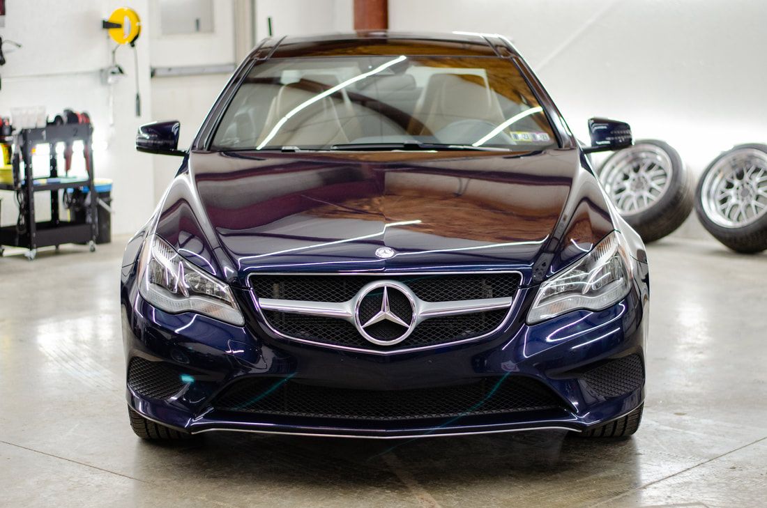 Dark blue Mercedes-Benz car with a chrome grill and logo, parked indoors.