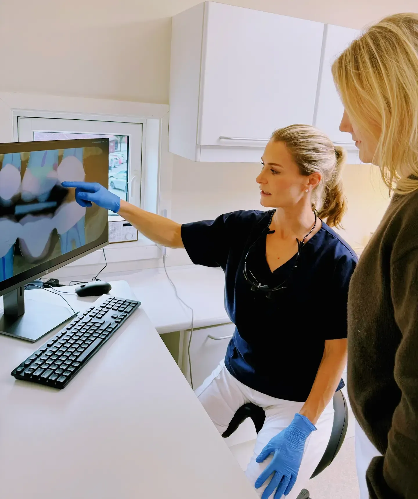 Tannlege peker på røntgenbilde på skjermen og forklarer til pasienten på et tannlegekontor.