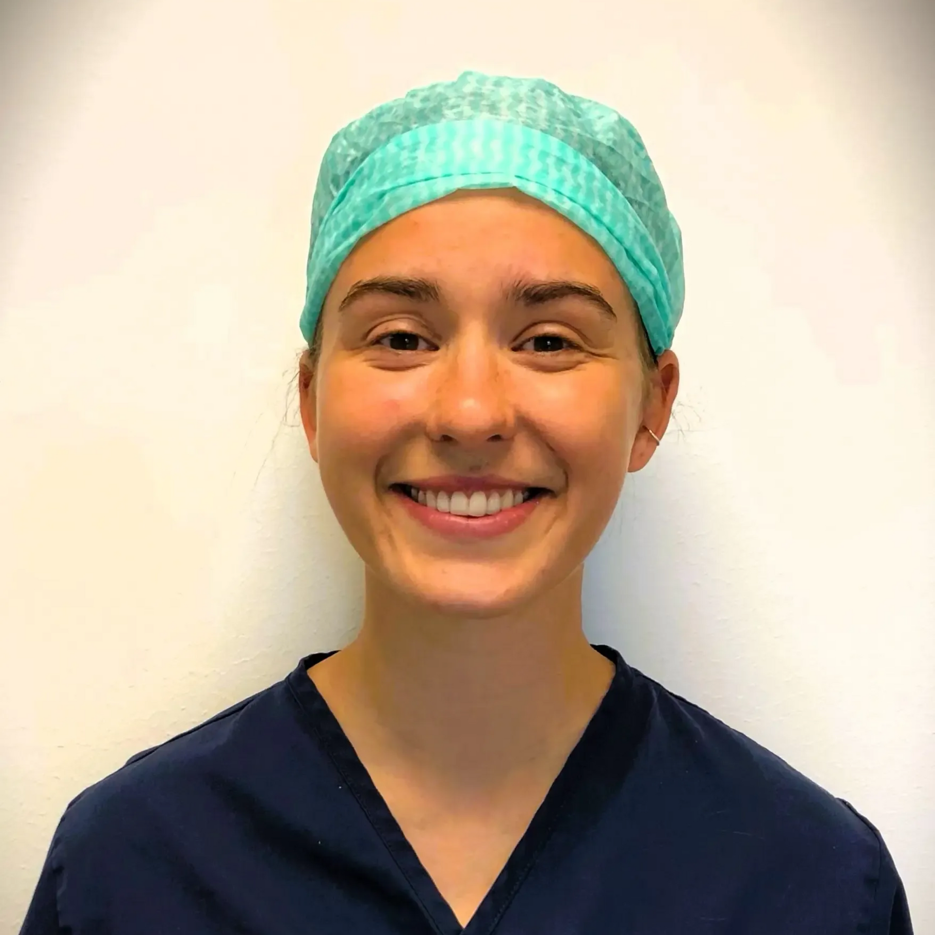 Kvinne i blå skrubber og operasjonshette smiler.