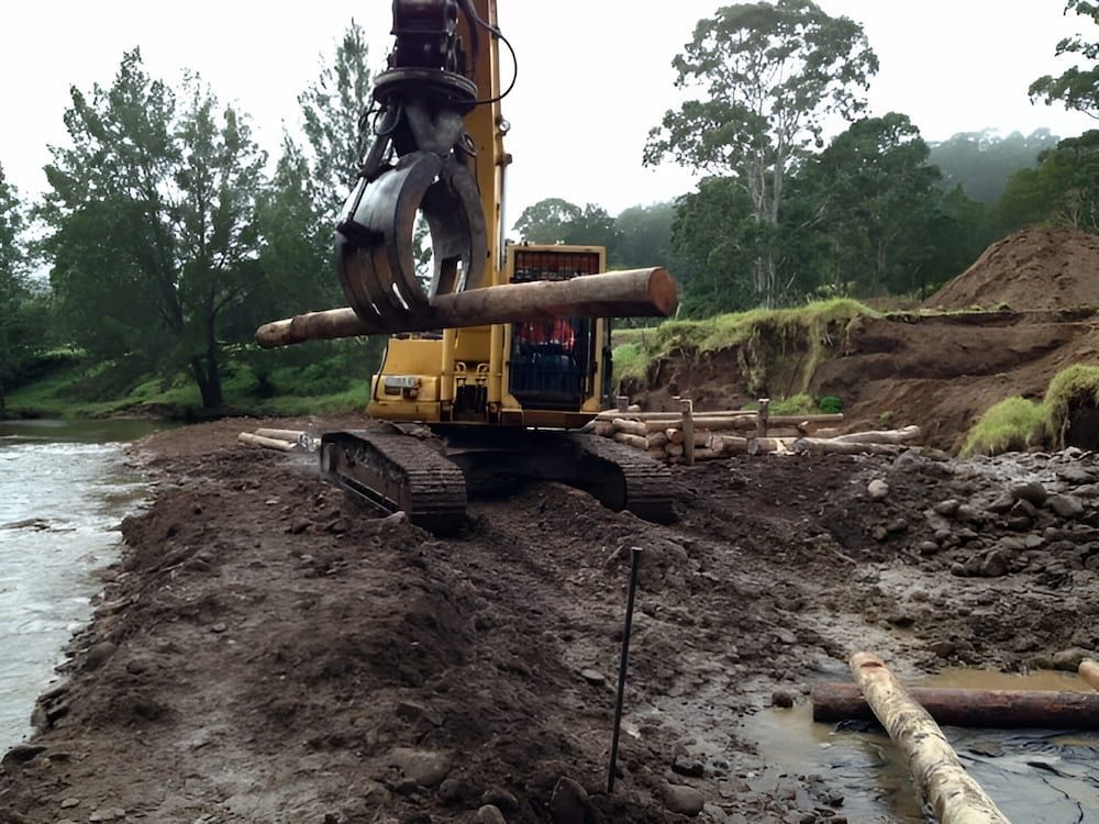 A Yellow Excavator is Digging in the Mud Near a River — Total Vegetation Management in Braemar, NSW