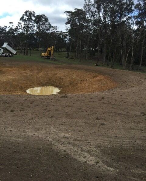 A Large Yellow Excavator is Sitting on Top of a Dirt Field — Total Vegetation Management in Braemar, NSW
