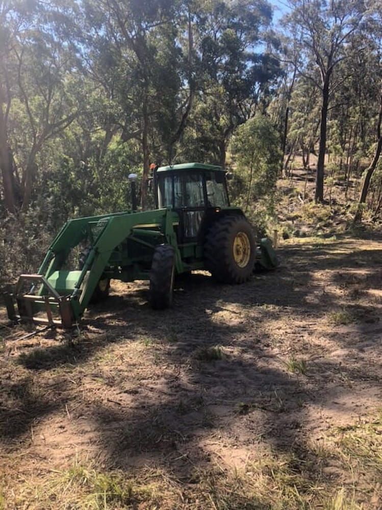 A Green Tractor is Parked in a Dirt Field in the Woods — Total Vegetation Management in Braemar, NSW