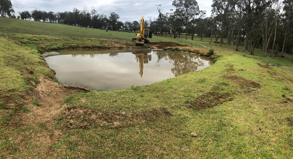 A Large Yellow Excavator is Working on a dam — Total Vegetation Management in Braemar, NSW