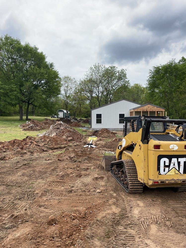 Yellow CAT bulldozer on a muddy construction site with a white house and trees in the background