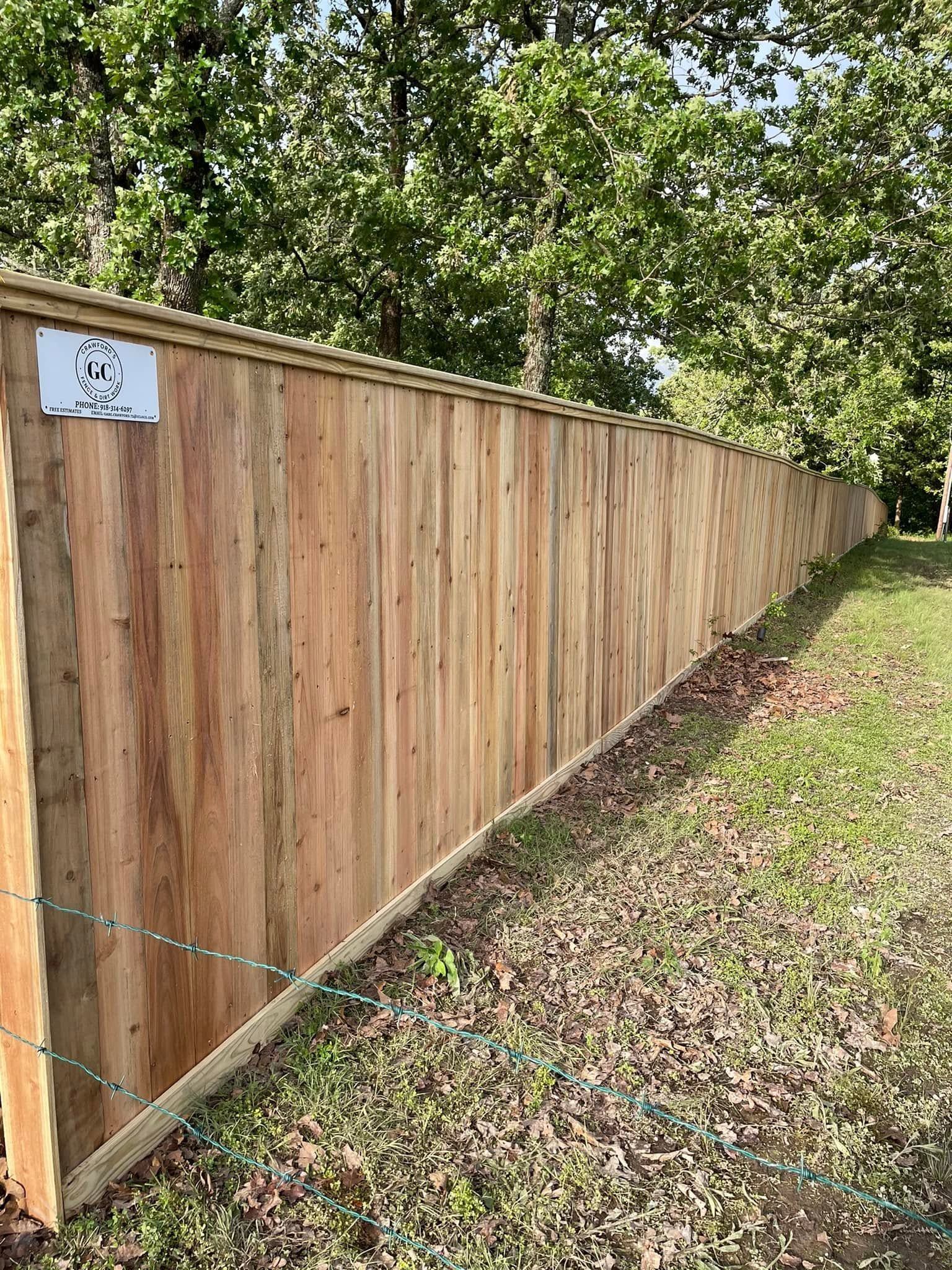 Long wooden privacy fence beside a grassy yard and trees, receding into the distance