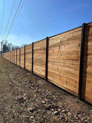Long wooden privacy fence beside a leaf-covered path under a clear blue sky