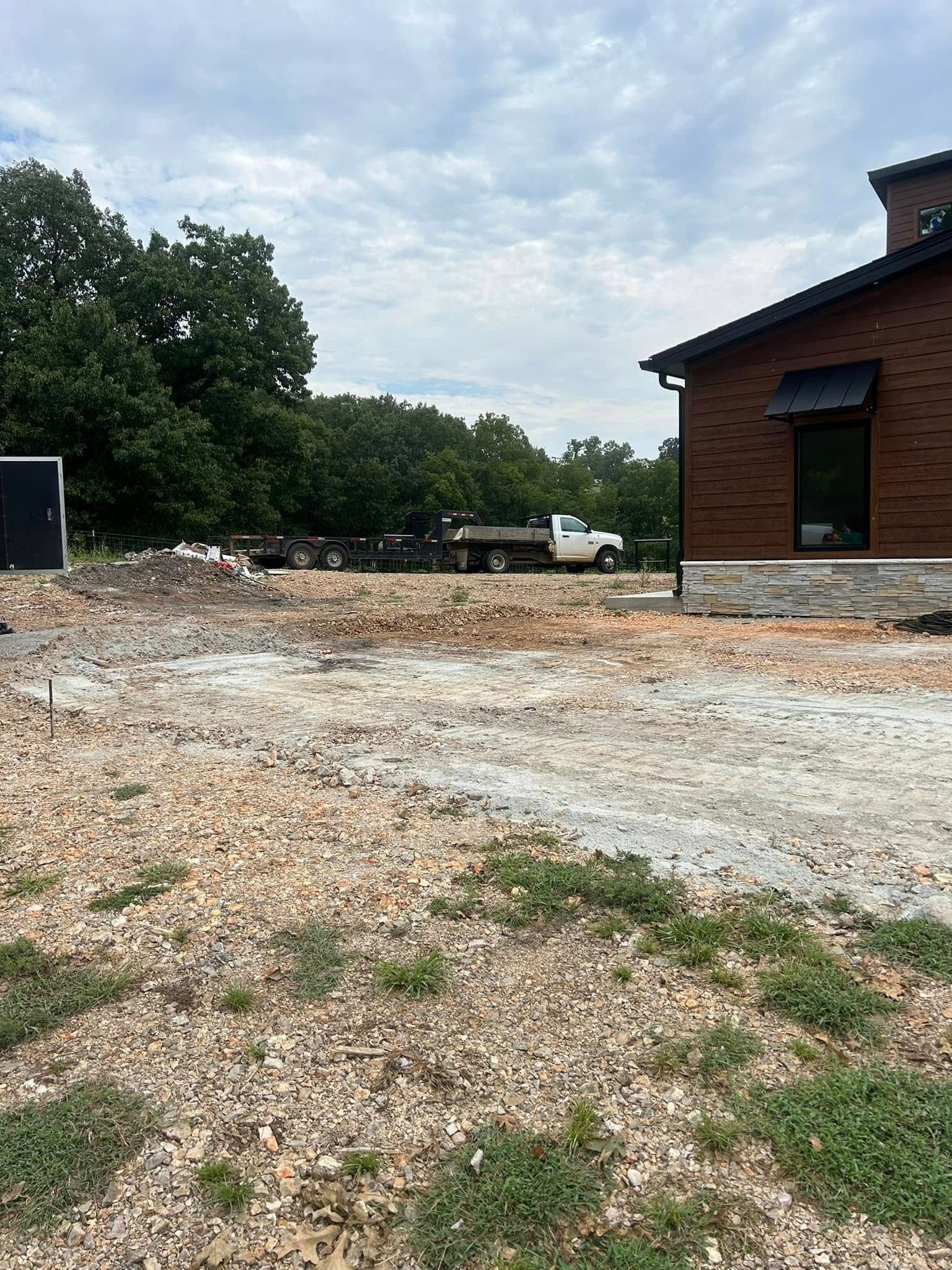 Gravel lot beside a brick building with trees and a cloudy sky in the background