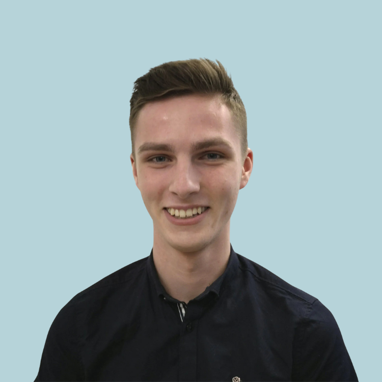 Young man with short brown hair smiles, wearing a dark blue button-up shirt against a light blue background.
