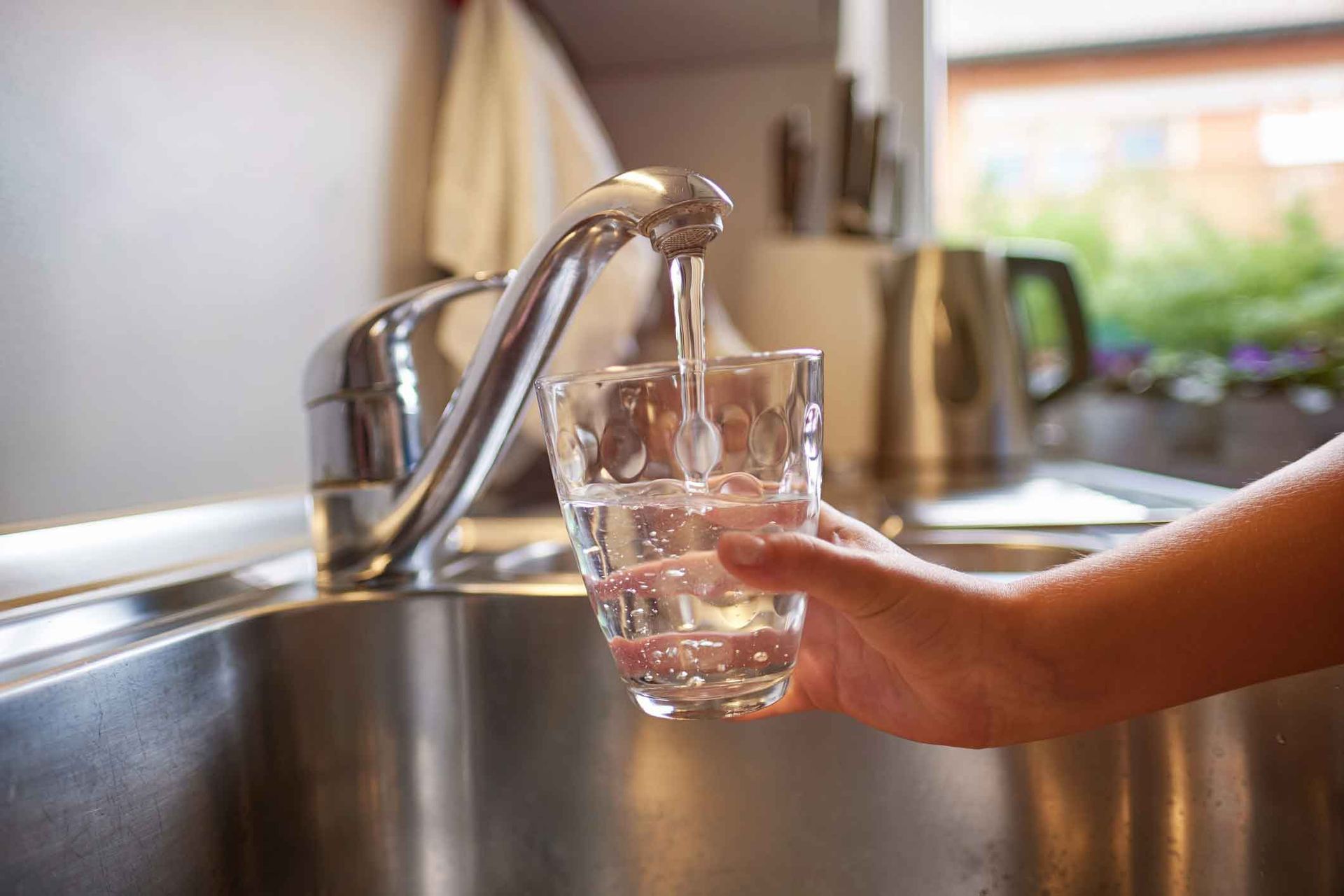 A person is pouring water into a glass from a faucet.
