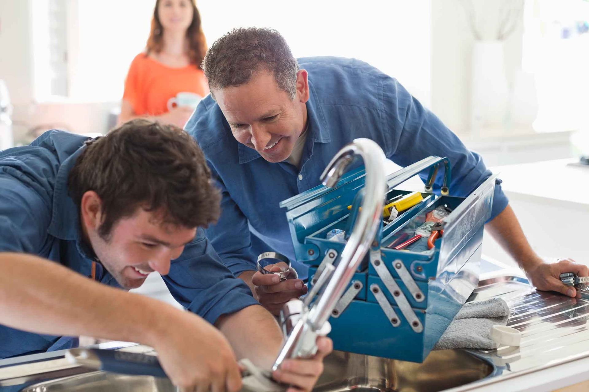 Two men are fixing a sink with a toolbox.