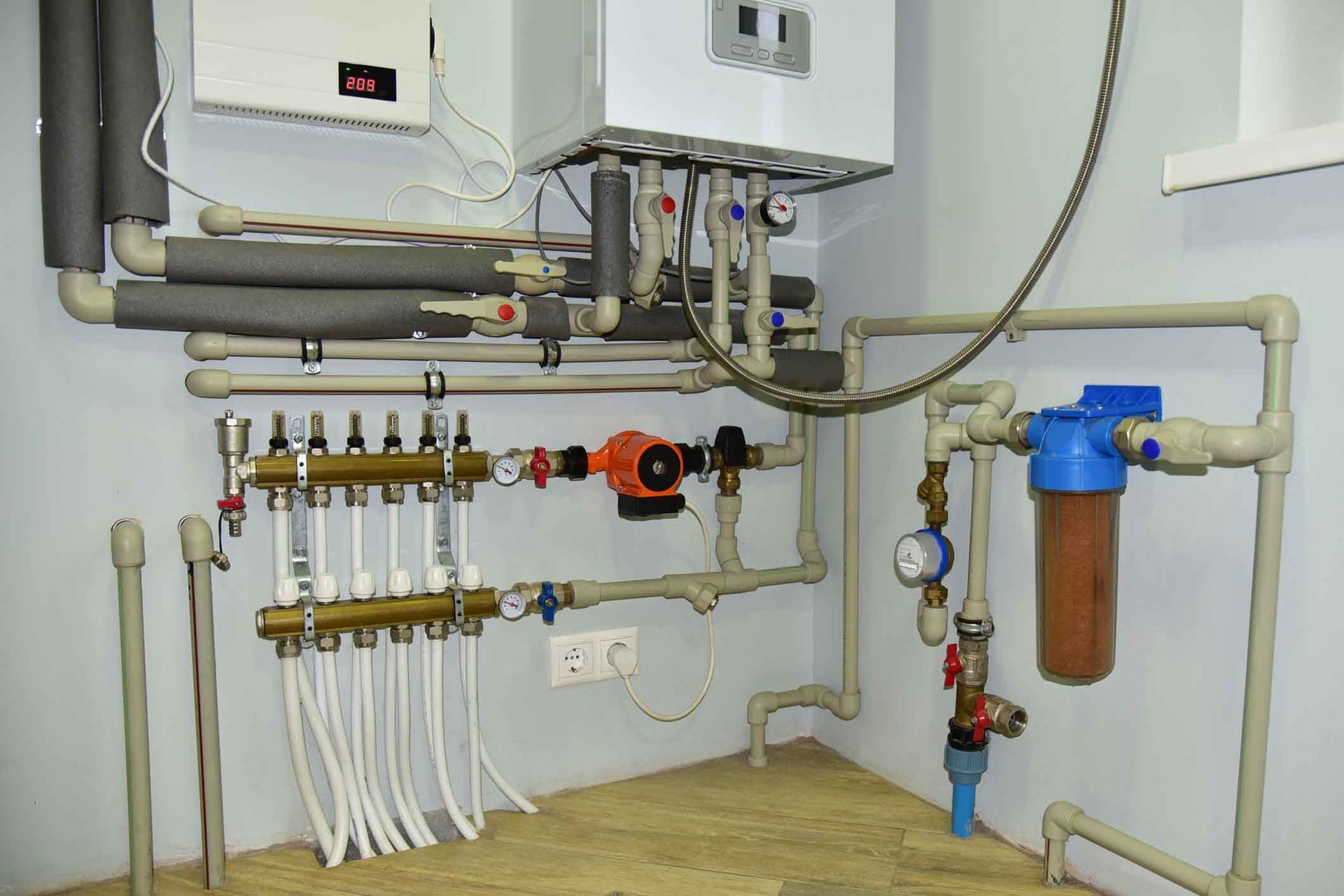 A room with a lot of pipes and a boiler on the wall.